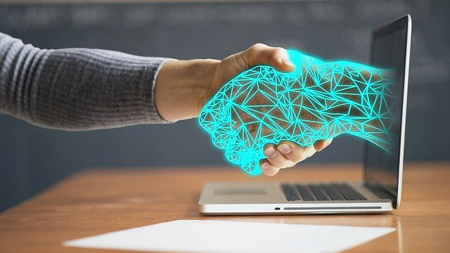En mänsklig hand tar i hand med en hand från en datorskärm